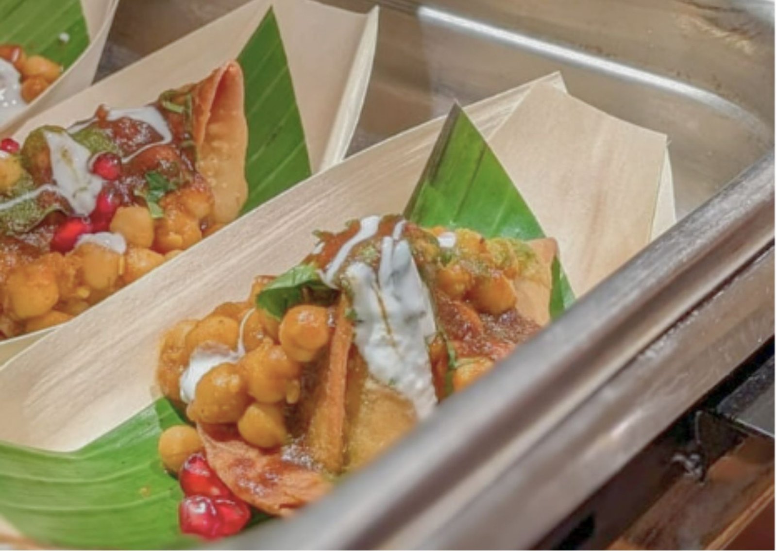 Close-up of two banana-leaf boats filled with chickpea fritters in sauce, topped with yogurt drizzle and herbs, ready to eat