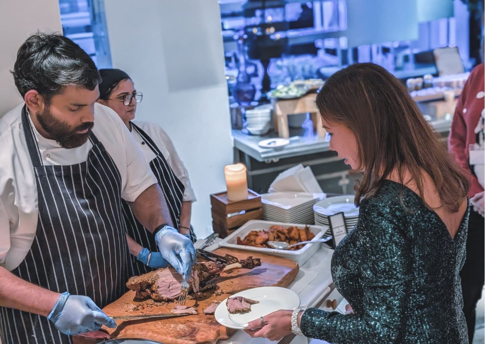 Chef in a striped apron carves roast beef for a guest at a buffet, slicing on a wooden board.