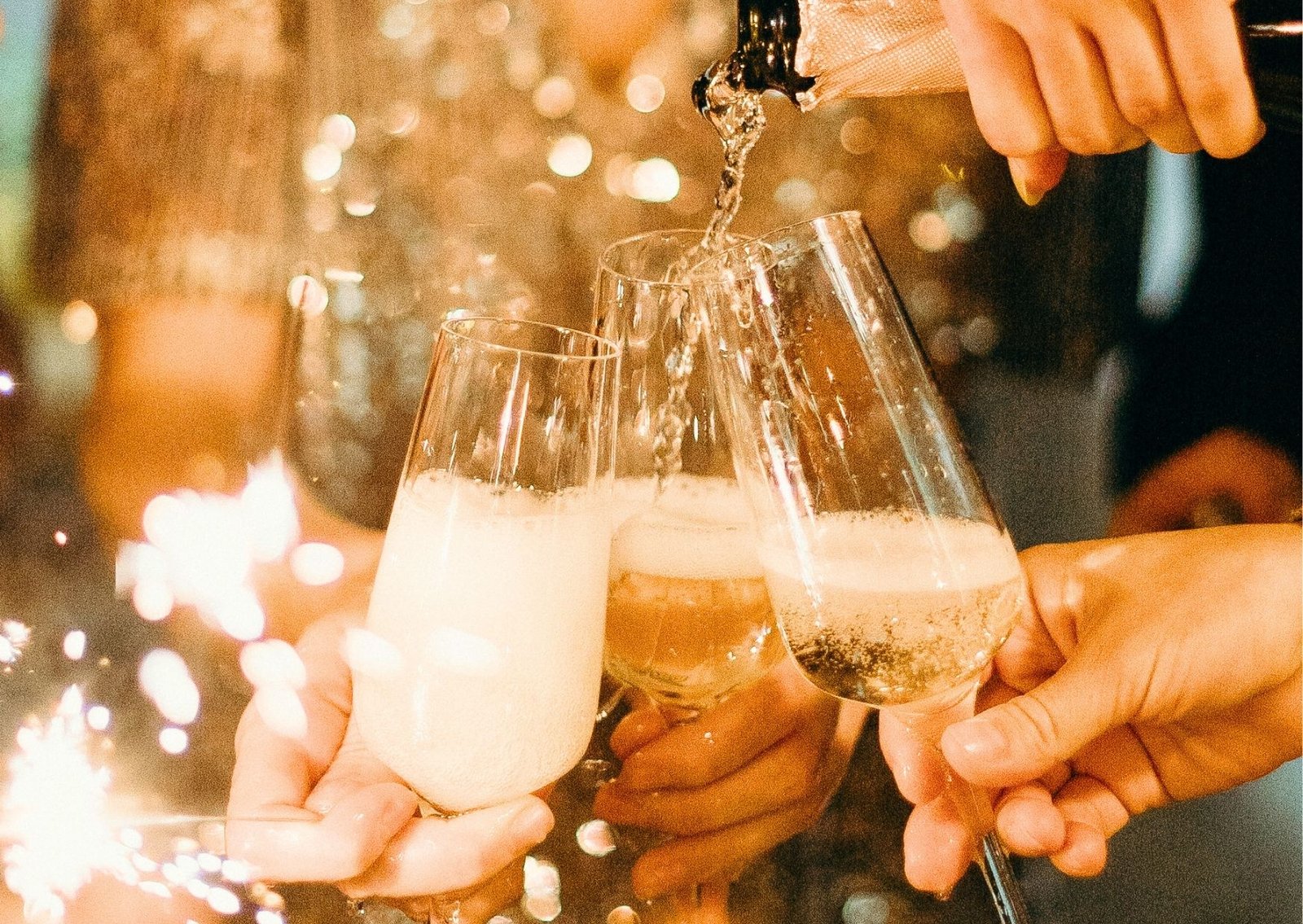 Group of people toasting with champagne flutes, warm bokeh lights in the background.