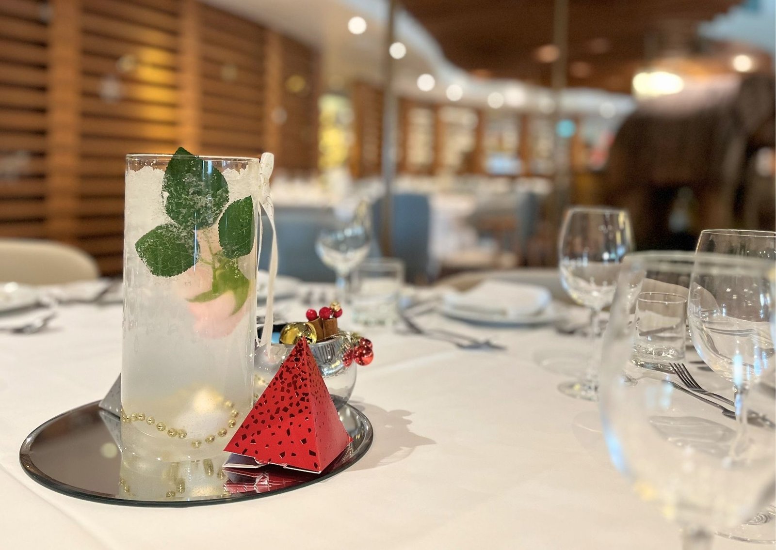 Frosted glass with mint leaves on a reflective charger, red party centerpiece on a white-table setting.