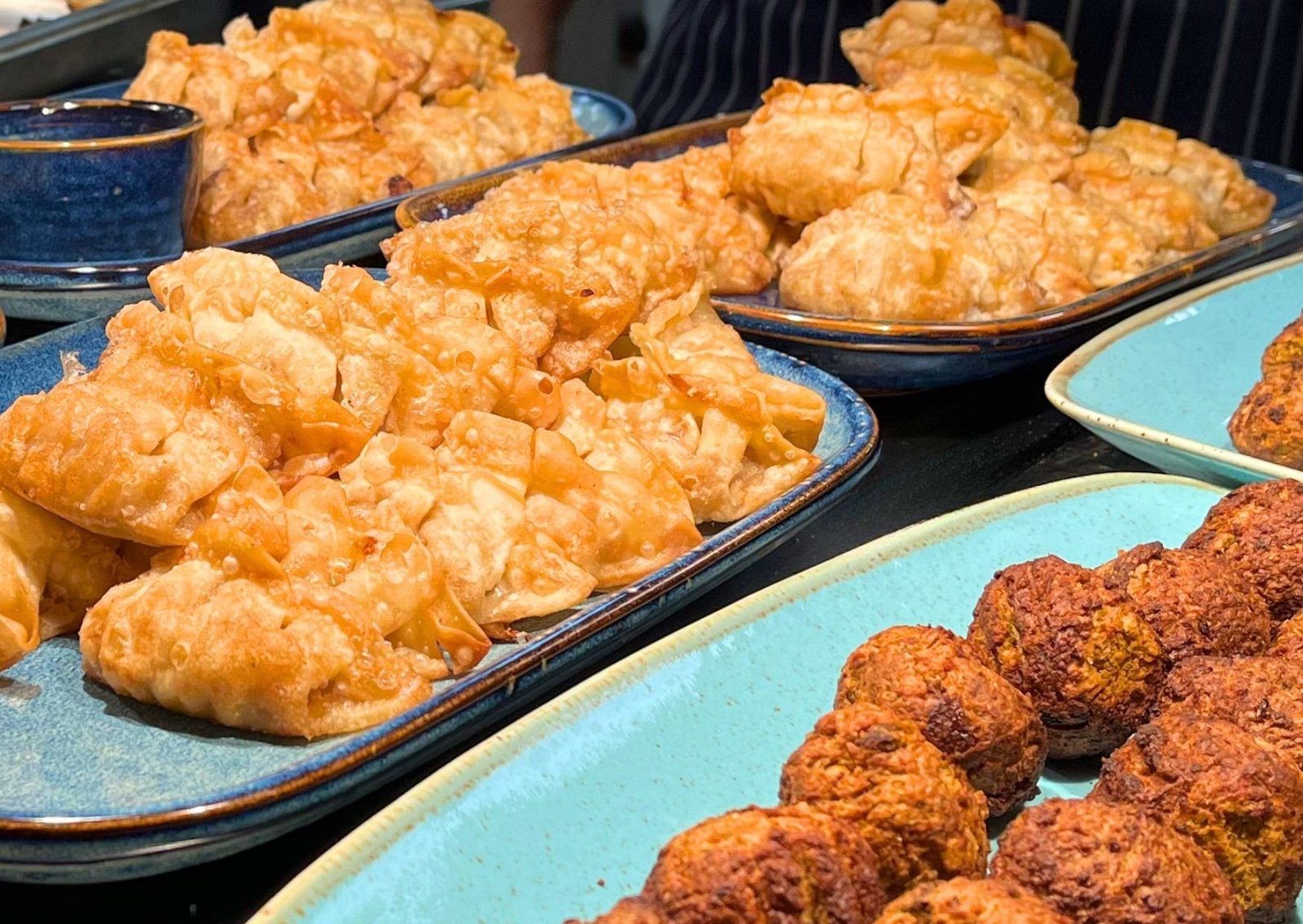 Crispy fried pastries piled on blue serving trays at a buffet.