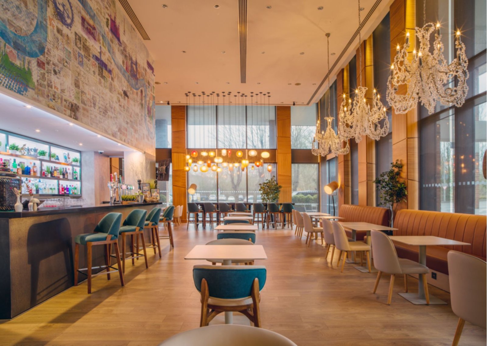Spacious cafe with a long bar on the left, teal stools, and chandelier lighting along the right side.