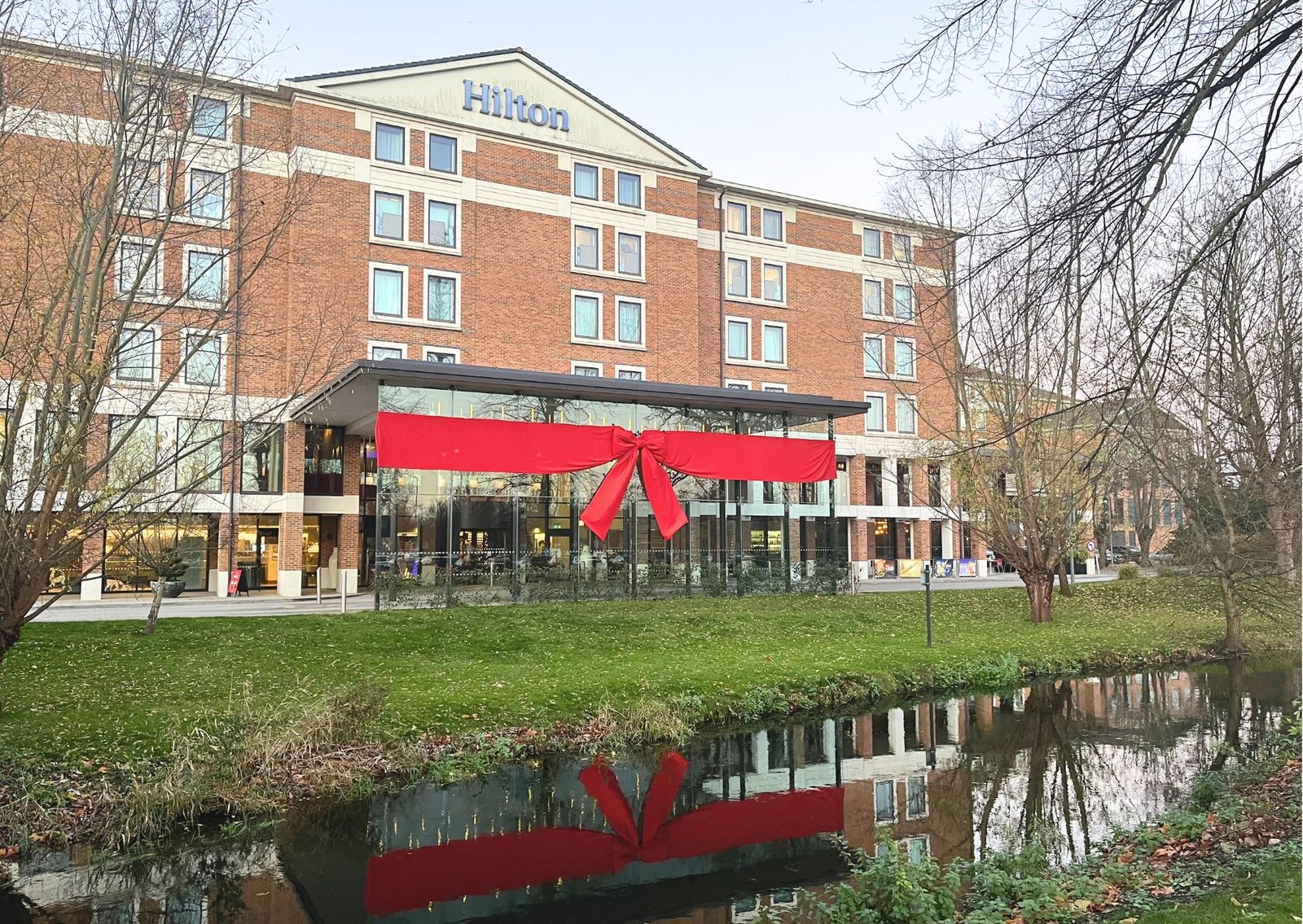 Hilton hotel with a large red ribbon across the main entrance, reflection visible in the adjacent canal.