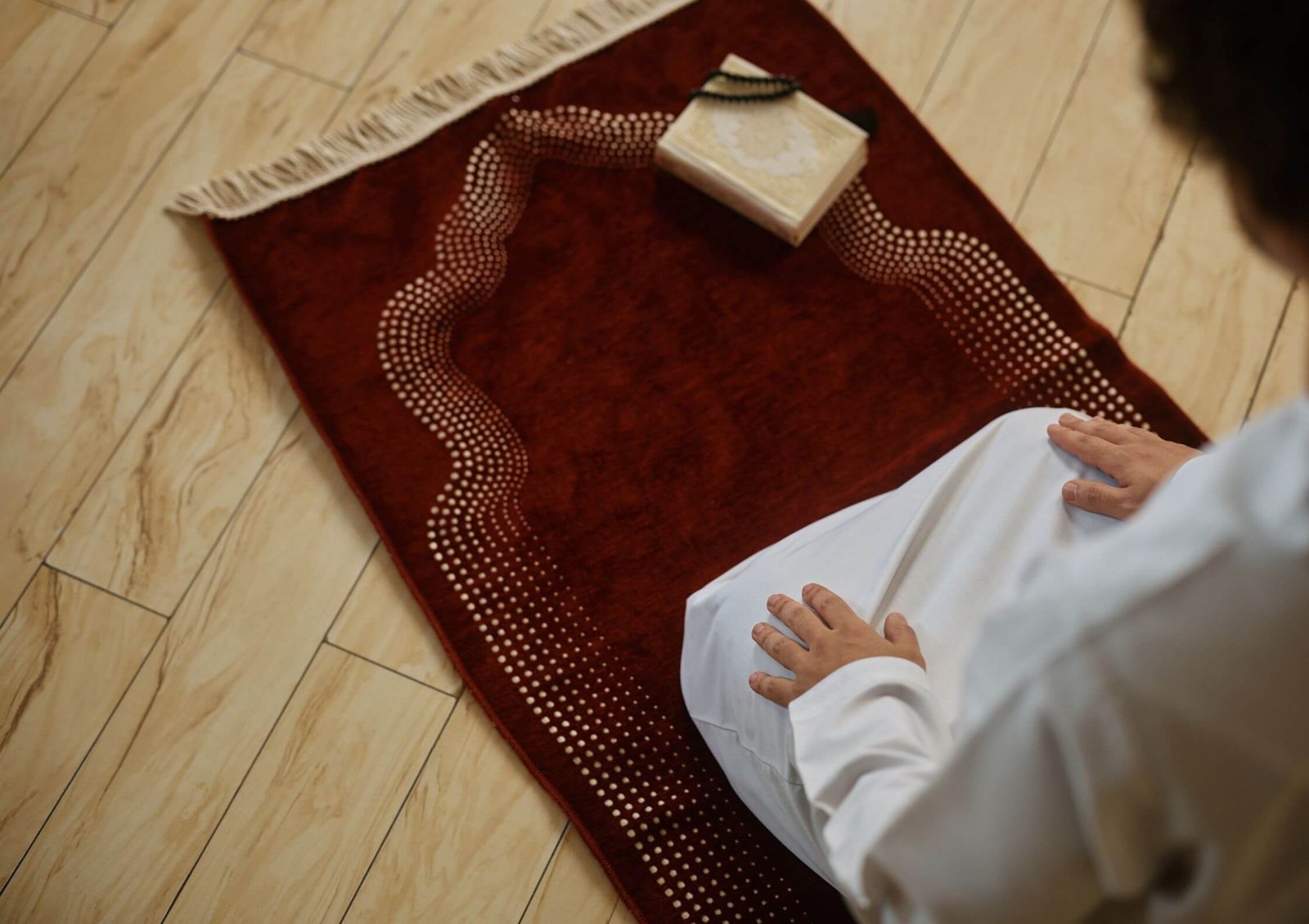 Person sitting on a red prayer rug with a small decorative box placed on it, hands resting on the knees.