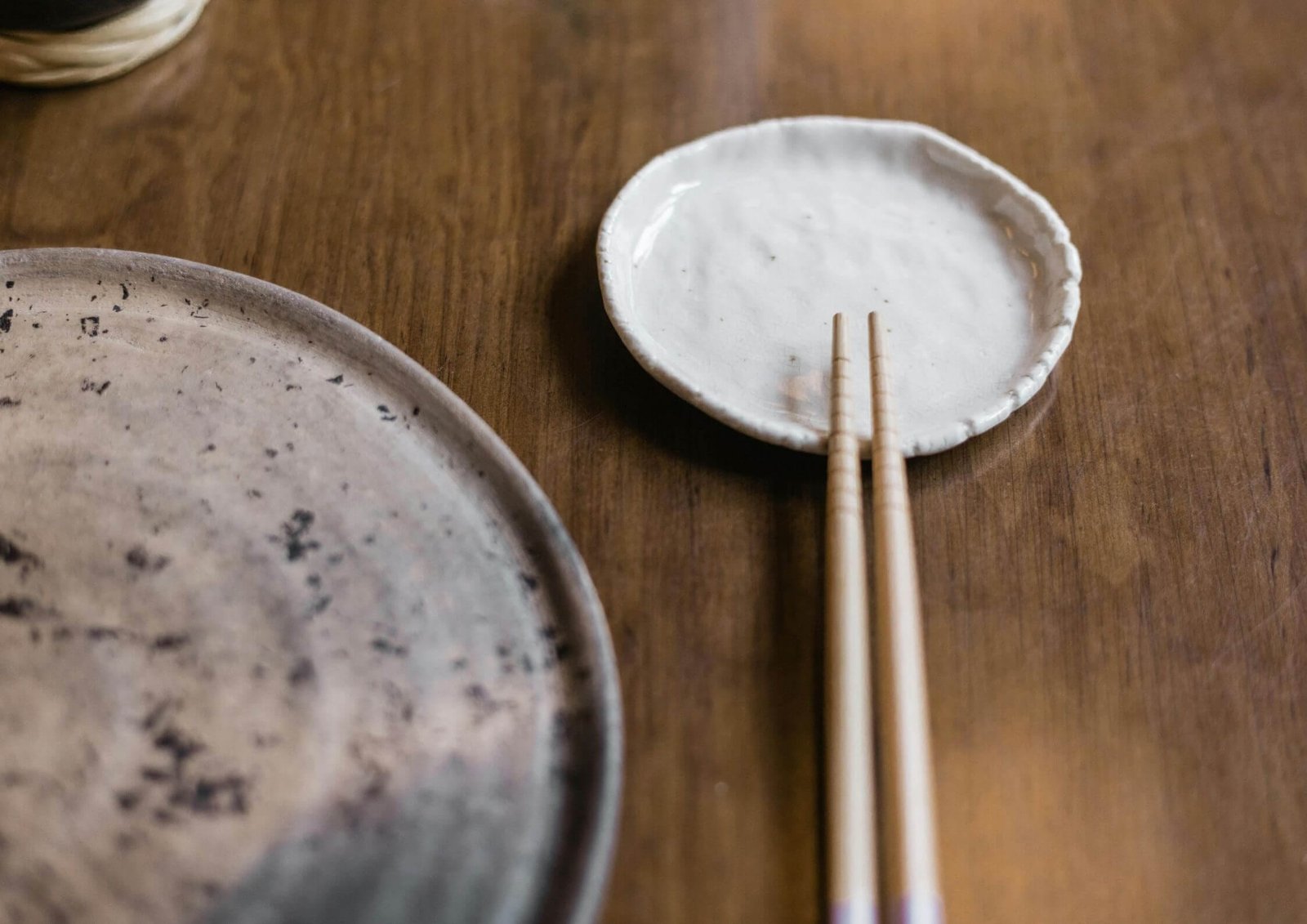 White speckled ceramic plate with chopsticks resting at its edge on a warm wooden table (partially showing another plate).