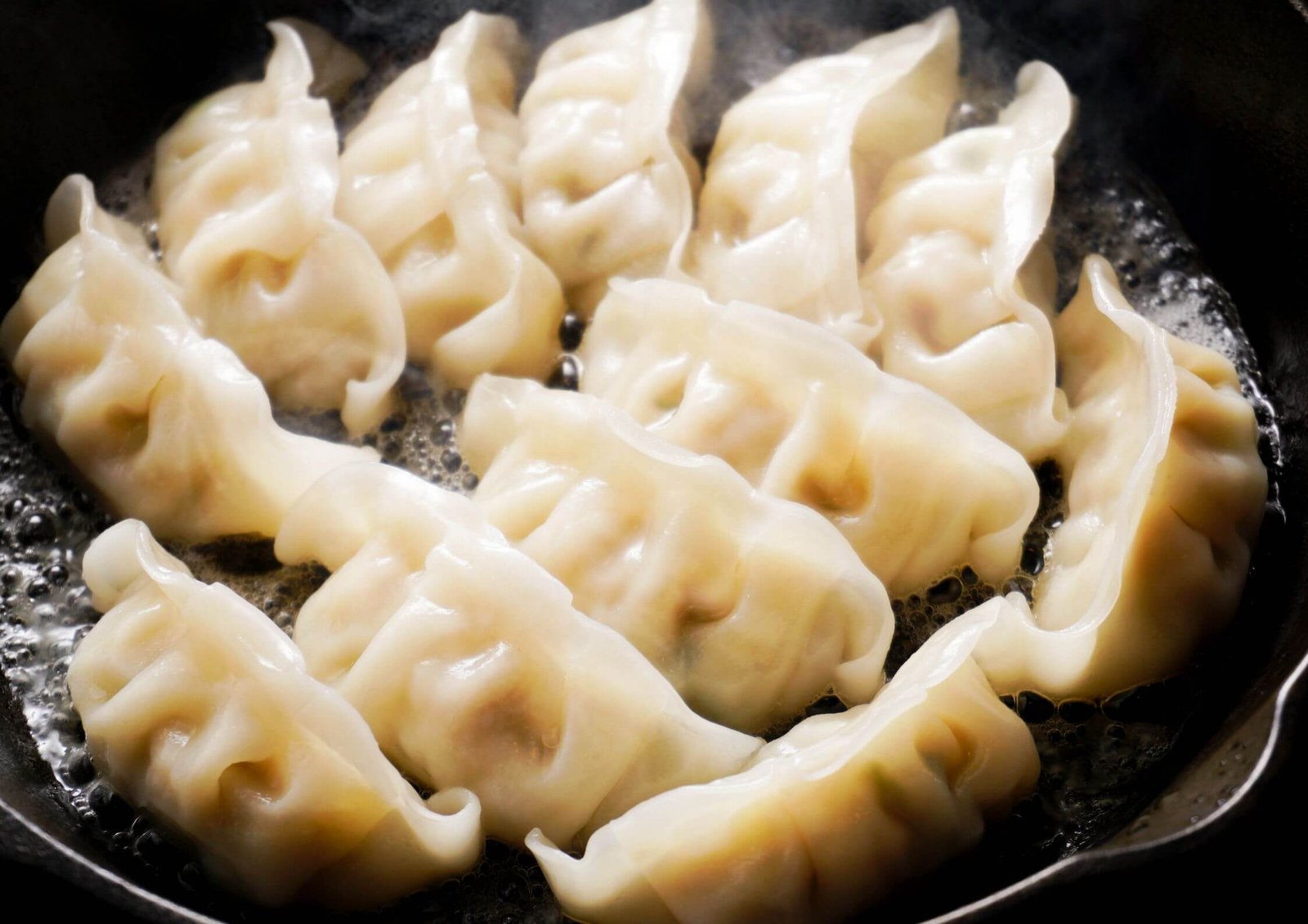 Close-up of crescent-shaped dumplings cooking in a hot pan, edges crispy and bubbling oil around them (potstickers).