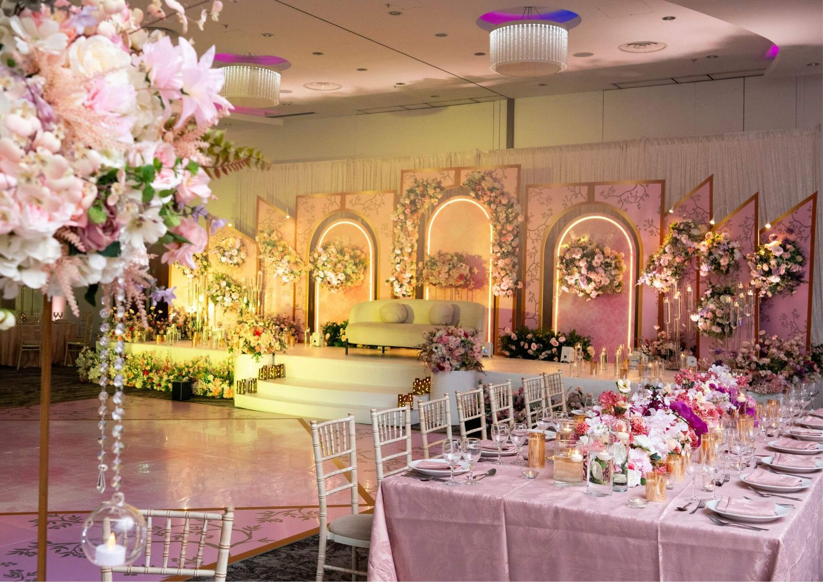 Elegant wedding reception setup with pink floral arches, candlelit tables, and soft pink tablecloths.