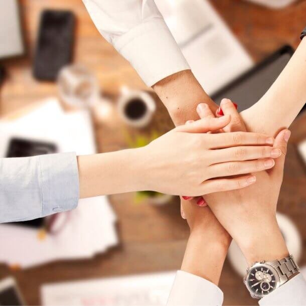 Hands stacked together in a teamwork gesture, symbolizing collaboration in an office setting.