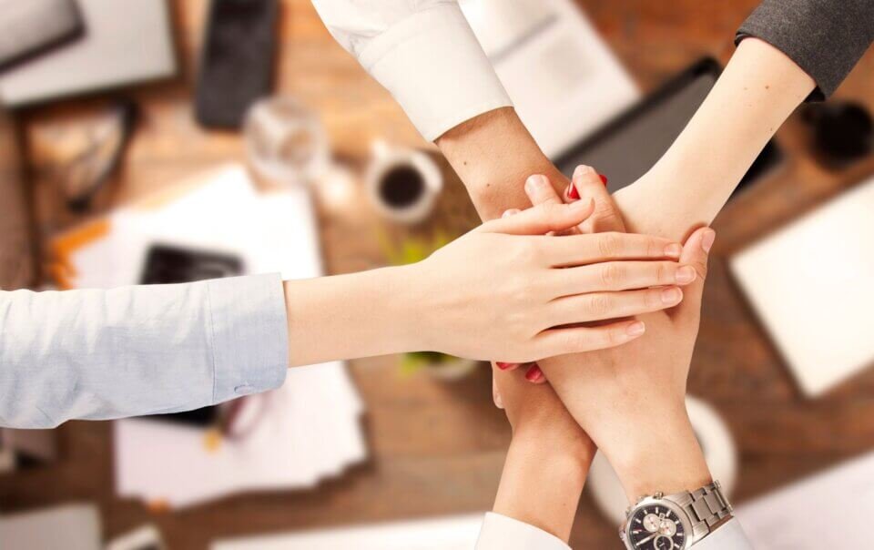 Hands stacked together in a teamwork gesture, symbolizing collaboration in an office setting.
