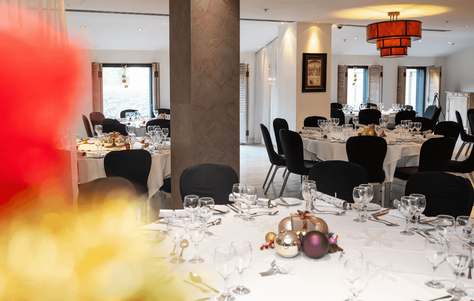 Banquet hall prepared for a formal dinner with round tables, white tablecloths, and glassware ready for guests; festive ornaments on the table centerpieces.