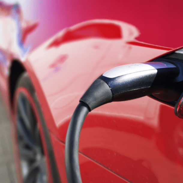 Close-up of a charging plug inserted into the side of a red electric car in the charging port area.