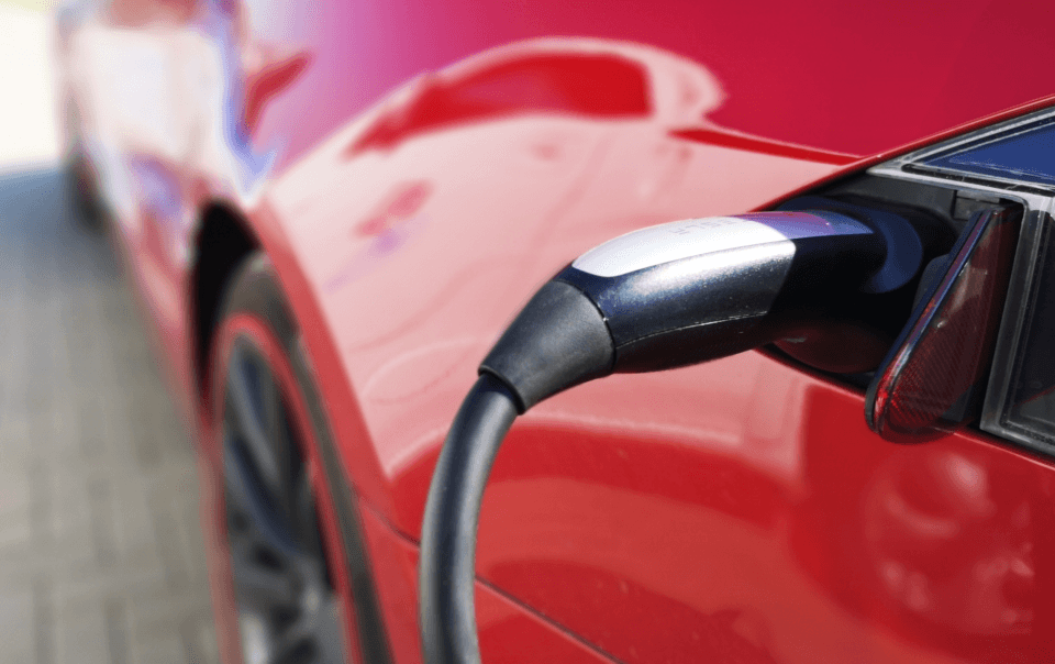 Close-up of a charging plug inserted into the side of a red electric car in the charging port area.