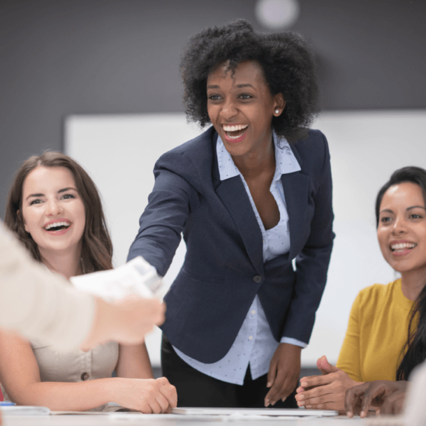 Group of diverse coworkers around a table, smiling and shaking hands in a collaborative meeting around documents and papers on the table.
