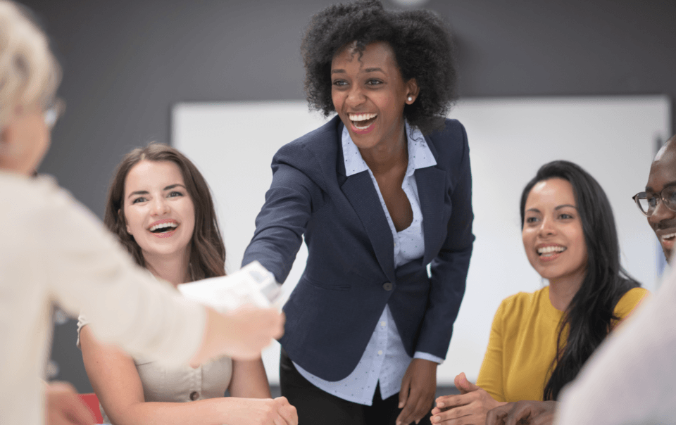 Group of diverse coworkers around a table, smiling and shaking hands in a collaborative meeting around documents and papers on the table.